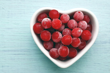 Frozen red viburnum berries in a white heart shaped bowl on a blue wooden background.Natural medicine,alternative treatment or health care concept.Selective focus.