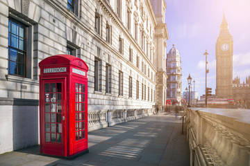Fototapeta na wymiar London, England - Traditional red British telephone box with Big Ben and Double Decker bus at the background on a sunny afternoon
