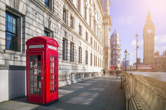London, England - Traditional red British telephone box with Big Ben and Double Decker bus at the background on a sunny afternoon