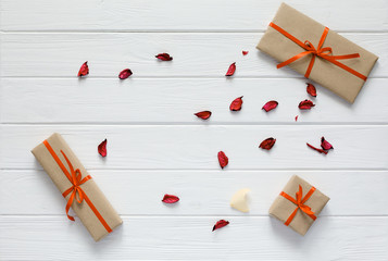Valentine Day Concept lovely wrapped in beige Color Paper and tied red Ribbon Gift Boxes of different Shape on white Wood Texture Background flat Lay top View Flower Petals randomly dropped copy space