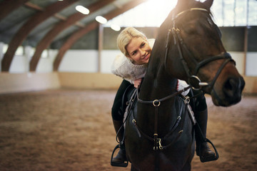 Smiling blonde female leaning on black horseback