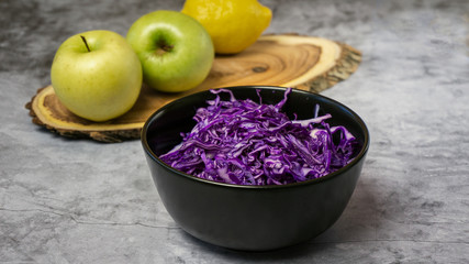 Shredded red cabbage with apples in black bowl on grey background. Vegetarian healthy food. Top view