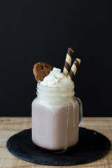 Portion of homemade hot chocolate with whipped cream, cookies and wafer sticks served on black slate board on wooden table