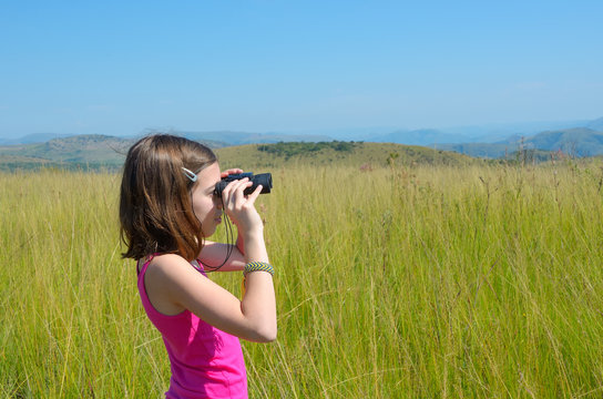 Child on safari travel in Africa,  girl looking to savannah with binoculars
