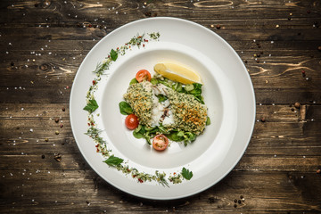fish steak with herbs, lemon, cherry tomatoes and spices on a white plate wooden background
