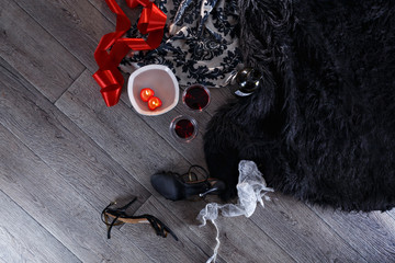 Two wine glasses, heart shaped candles, lingerie scattered in a party aftermath on silk and fur on floor