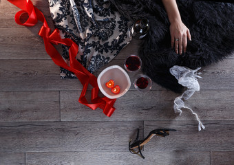 Two wine glasses, heart shaped candles, lingerie scattered in a party aftermath on silk and fur, female hand rest on fur