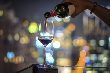 Wine glass with red wine decant from bottle in city bokeh background