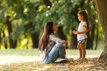 Mother sitting with her daughter and playing around the park on a beautiful morning.	  - obrazy, fototapety, plakaty