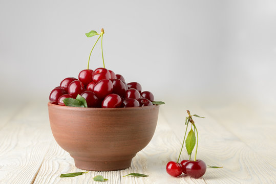 ripe cherries and leaves in a bowl on a textured wooden background