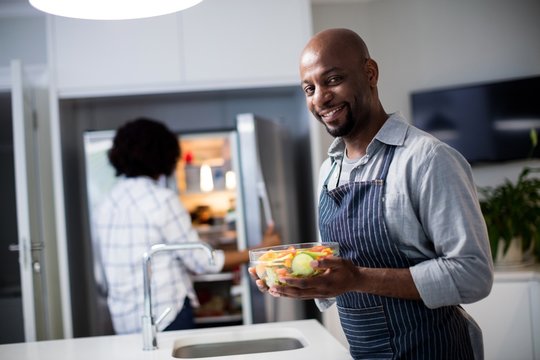 Portrait of man holding bowl of salad while woman opening a refr