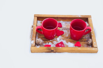 Two red cups with tea on a wooden tray in snow. Romantic Valentine's day winter picnic, hot tea, couple. Lifestyle, time together outdoors. Snowflakes, hoarfrost, heart shape on a tray