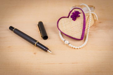 Elegant valentine background with white pearls and gift box shaped of heart and black fountain pen on wooden background