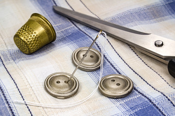 Buttons, needle with thread, thimble and scissors on fabric background