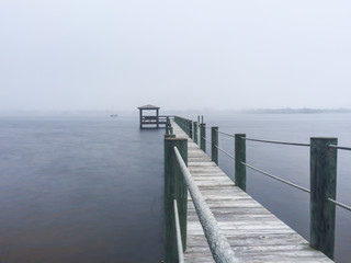 Obraz premium Pier on a river in a foggy morning with a sailboat in the background