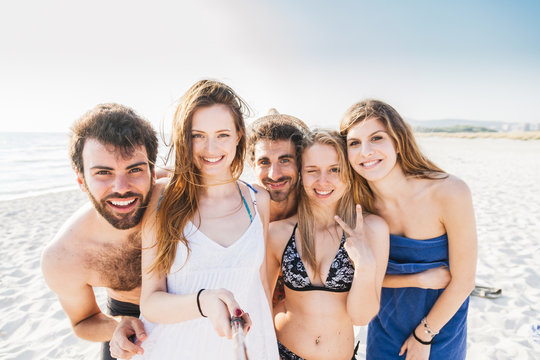 Selfie on the beach, summer day at sunset. Five friends in swimwear, two men and three women take photo near sea
