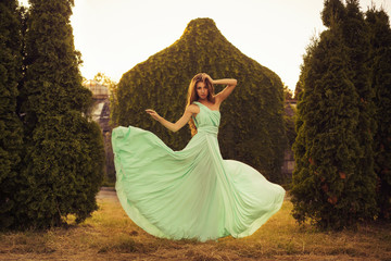 Beautiful blonde with a long curly hair in a long evening dress in motion outdoors near retro...