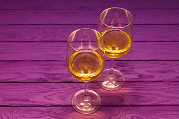White wine in the wineglass on the purple wood background