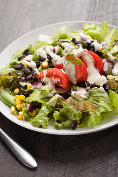Angled shot of black bean, corn, and tomato southwest salad on a dark wooden background