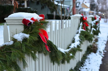 Snow covered evergreen garland draped along a white picket fence