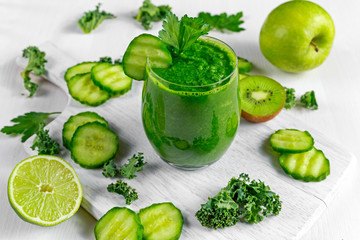 Fresh Green smoothie with kale, cucumber, lime, apple, parsley on white board.