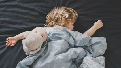 Маленький малчьик спит в кроватке с игрушкой