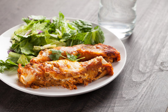 Spicy chicken enchiladas with a side of light green salad on a dark wood background horizontal shot