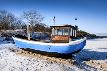 Germany, Usedom: Blue white striped fishing boat on snowy beach.