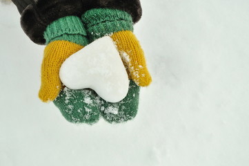 Female hands in knitted mittens with heart of snow in winter day. Love concept. Valentine day background. 