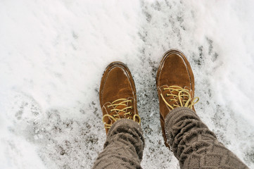 Female feet in shoes on the snowy pavement.