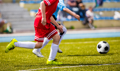 Children Soccer Players Running with the Ball. Kids in Red Soccer Jerseys Playing Football on the Pitch. Sports Stadium in the Background © matimix