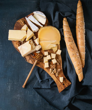 Cheese plate. Assortment of cheese with walnuts, honey and bread on olive wood serving board with textile over dark blue canvas as background. Top view with space.