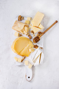 Cheese plate. Assortment of cheese with walnuts and honey from honey dipper on white wood serving board over white concrete texture background. Top view with space. Appetizer theme