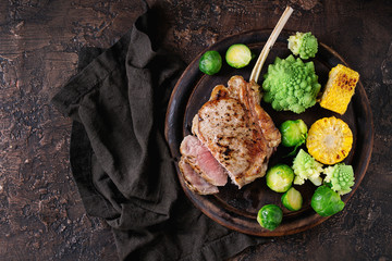 Sliced Grilled veal tomahawk steak with vegetables brussels sprouts, romanesco and corn cobs served on wooden serving chopping board over old wood background. Top view with space.  - obrazy, fototapety, plakaty