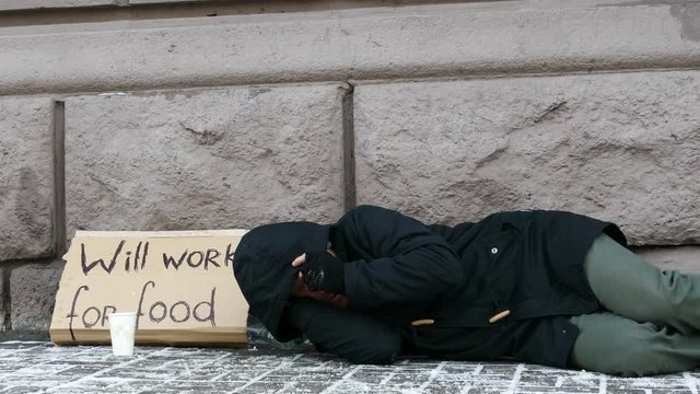 
4K.  Homeless  adult man  lie in  city winter  street, unemployment  beggar symbol
