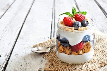 Healthy blueberry and raspberry parfait in a mason jar on a rustic white wood background - obrazy, fototapety, plakaty
