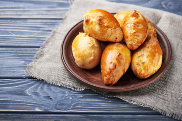 Delicious rustic pastries filled with meat and vegetables on a ceramic plate with wooden on a wooden background.