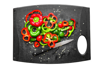 Cutting board and knife with fresh organic red and green bell peppers sliced and chopped for meal preparation on isolated white background