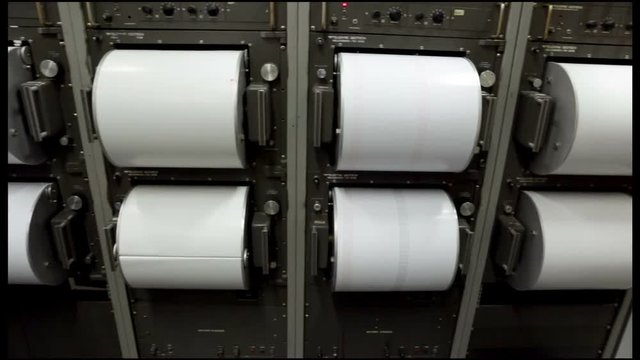 Seismograph records an earthquake on the sheet of measuring paper. Seismological device for measuring earthquakes. Seismograph machine needle drawing a red line on graph paper measuring activity. Pan.