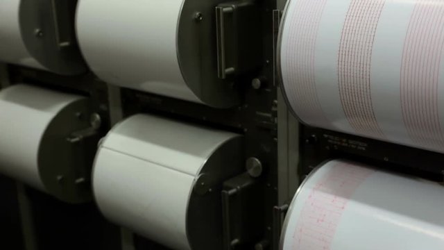 Seismograph records an earthquake on the sheet of measuring paper. Seismological device for measuring earthquakes. Seismograph machine needle drawing a red line on graph paper measuring activity.