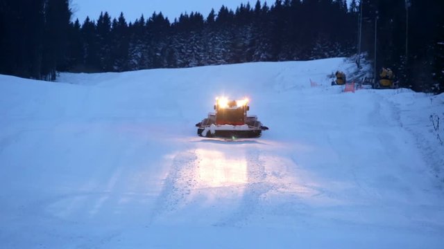 Snow plow truck on a ski slope levels up the snow for the ski and snowboard riders for the night.