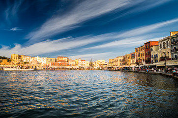 CHANIA, CRETE - JUNE 26, 2016: View of the old venetian port of Chania on Crete island, Greece. Tourists relaxing on promenade.