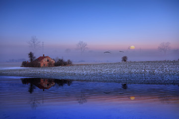 Stary dom o zachodzie słońca nad jeziorem zimą. © Stanisław Błachowicz