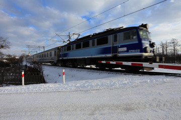 Pociąg osobowy na przejeździe kolejowym z opuszczonymi rogatkami.
