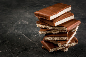 Stack of pieces of chocolate filled with white nougat on a dark stone table, copy space
