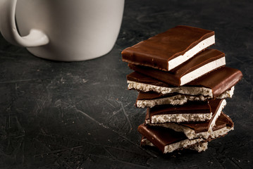 Stack of pieces of chocolate filled with white nougat on a dark stone table, with cup of tea, copy space