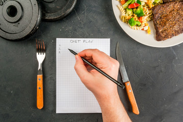 Concept of dieting, counting calories: a plate of healthy food (whole grain pasta with vegetables); man fills out a food diary. Hands in picture, top view, copy space