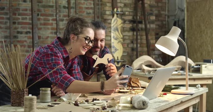 Selfie With the Master/A day at work with no selfie? No, thanks! Young hipster girl takes selfie with a mature master. They obviously work together in a workshop
