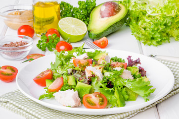 Fresh salad with chicken, avocado, tomatoes and flax seeds on a plate on white wooden background. Healthy food.