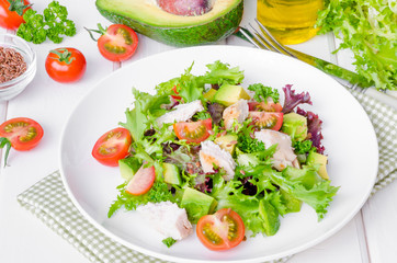 Fresh salad with chicken, avocado, tomatoes and flax seeds on a plate on white wooden background. Healthy food.